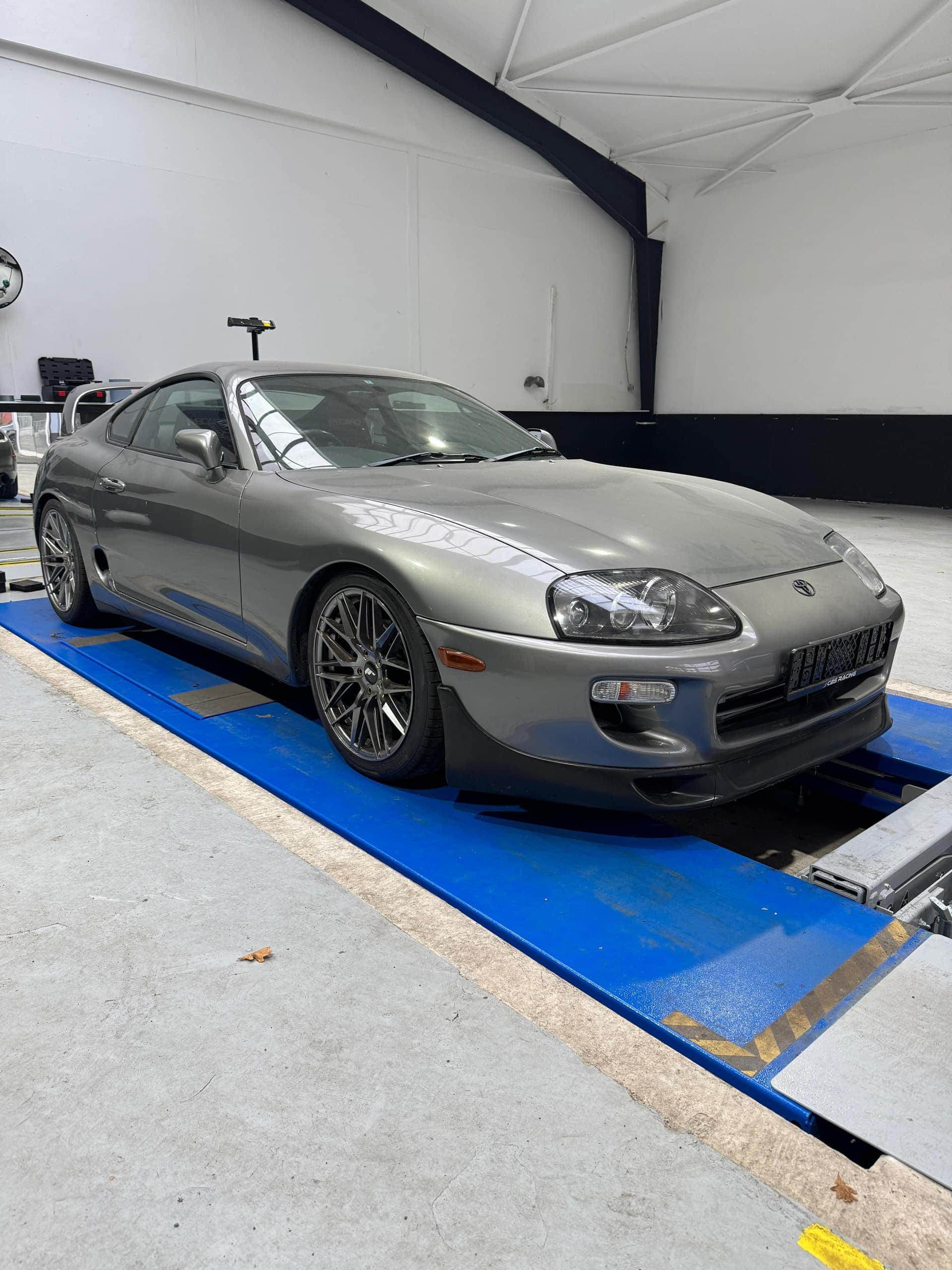 Grauer Toyota Supra im Dreiviertelprofil auf der blauen Hebebühne der Prüfhalle