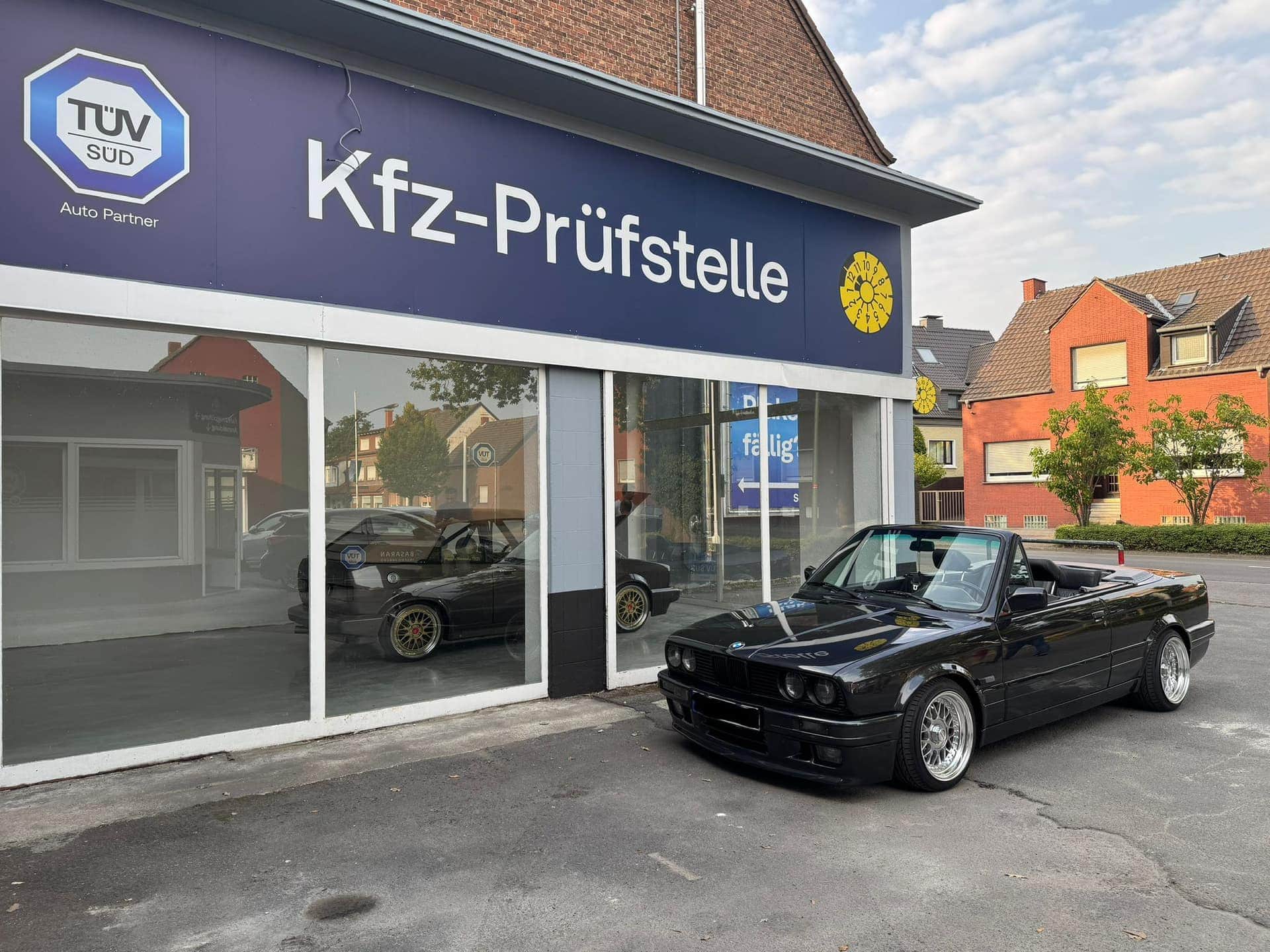 Schwarzes BMW-Cabrio auf dem Hof vor der Kfz-Prüfstelle Basaran, darüber das blaue Schild mit TÜV-SÜD-Zeichen
