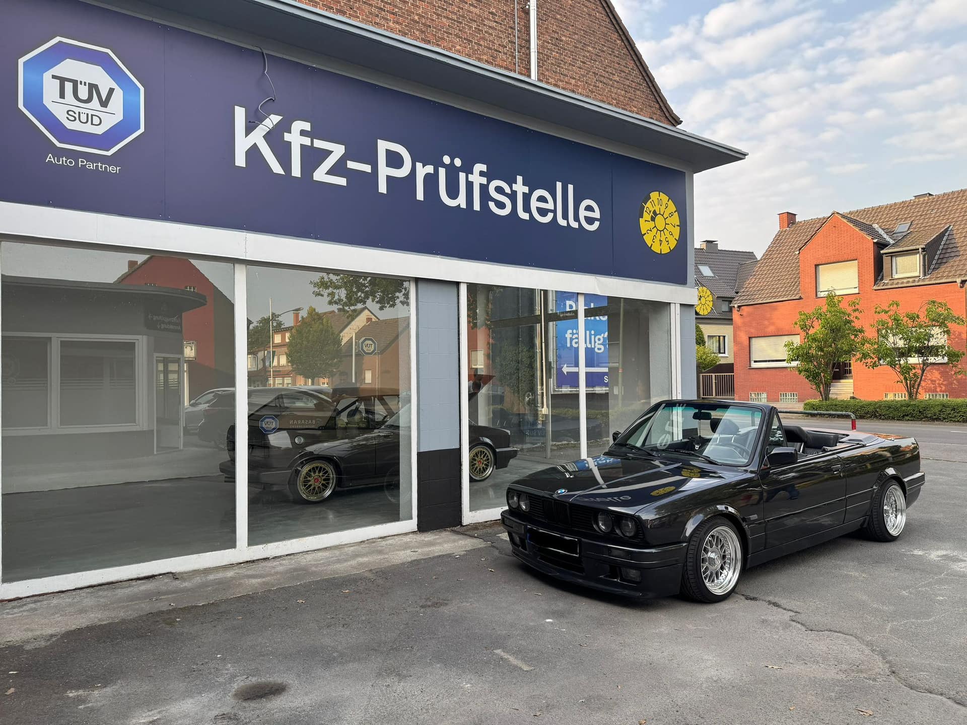Schwarzes BMW-Cabrio auf dem Hof vor der Kfz-Prüfstelle Basaran, darüber das blaue Schild mit TÜV-SÜD-Zeichen